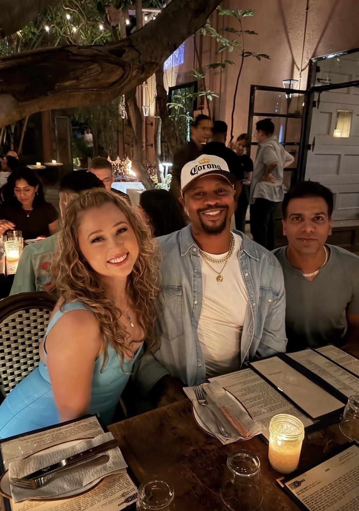 Three guests seated together at a Rise Up Collective dinner under string lights